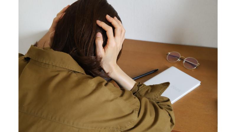 頭を抱えて悩む女性の後ろ姿