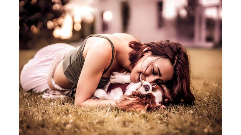 草むらに寝転んで抱き合う飼い主の女性と犬