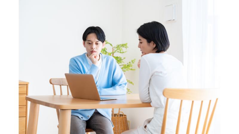 ダイニングテーブルで向かい合ってパソコンを眺める夫婦