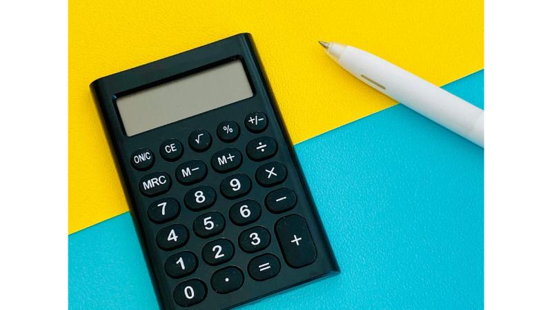 2色に分かれた背景の上に置かれた黒い電卓と白いボールペン