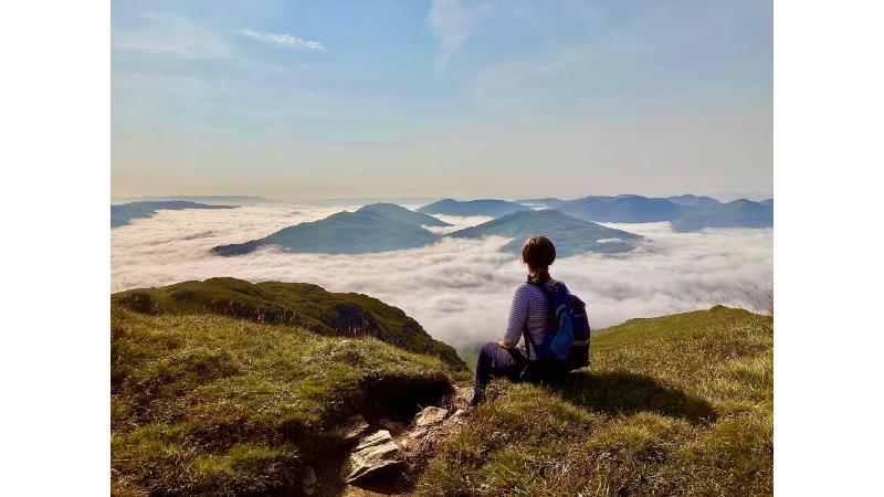 山の頂上で雲海を見つめる女性の後ろ姿