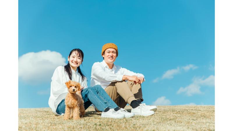 青空の下で座る男女とトイプードル
