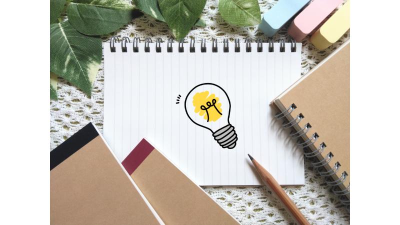 ノートに描かれた電球の絵と周りに置かれた付箋やノート